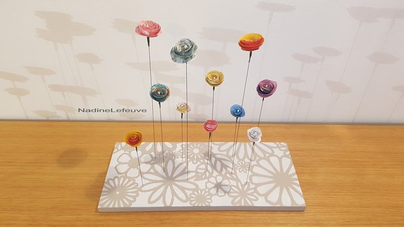 Objet décoratif composé de fleurs en papier d'origami montées sur de fines tiges métalliques et présentées sur un linéaire en bois peint réalisée par Nadine Lefeuve.